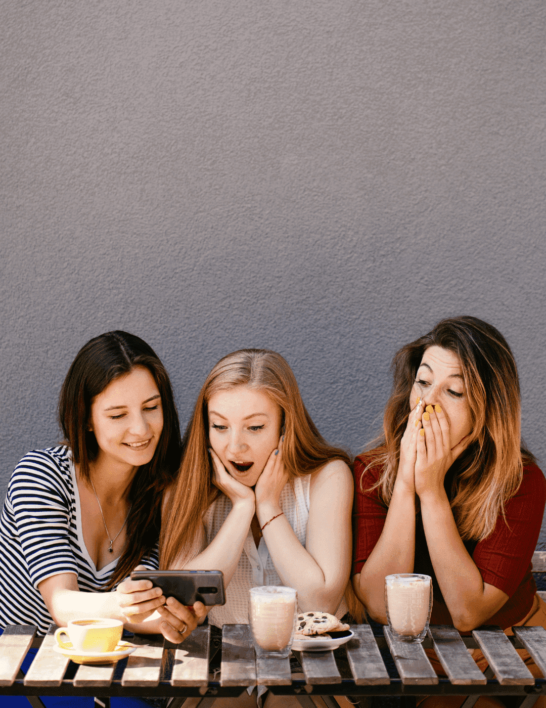 Hier auf dem Bild sieht man drei junge Frauen die an einem kleinen Tisch sitzen, einen Kaffee genießen und dabei Fun Facts zum Thema Englisch lernen lesen.