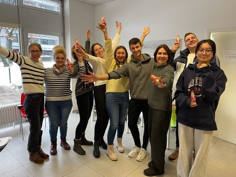 Eine Gruppe von Schülerinnen und Schülern feiert drinnen, lächelnd und mit kleinen Schokoladenweihnachtsmännern in der Hand.