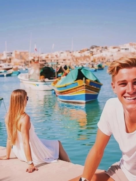 Girl sitting by the harbour in Malta, overlooking colourful traditional boats in the clear blue water.