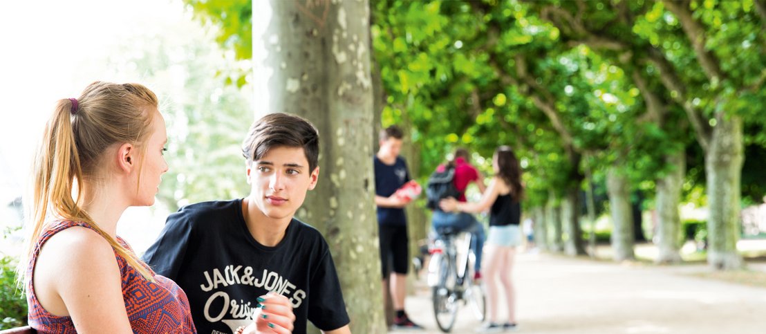 Hier lernen zwei Sprachschüler in Frankfurt schöne deutsche Wörter. Sie verbringen eine entspannte Zeit in einem frankfurter Park und unterhalten sich auf Deutsch.