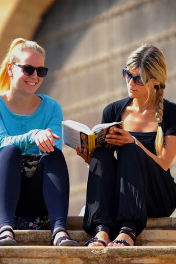 Zwei Sprachcaffe-Schülerinnen sitzen auf einer Treppe in Rabat, Marokko, und lesen und unterhalten sich vor einer traditionellen Architektur.