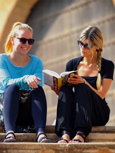 Two Sprachcaffe students sitting on steps in Rabat, Morocco, reading and chatting in front of traditional architecture.