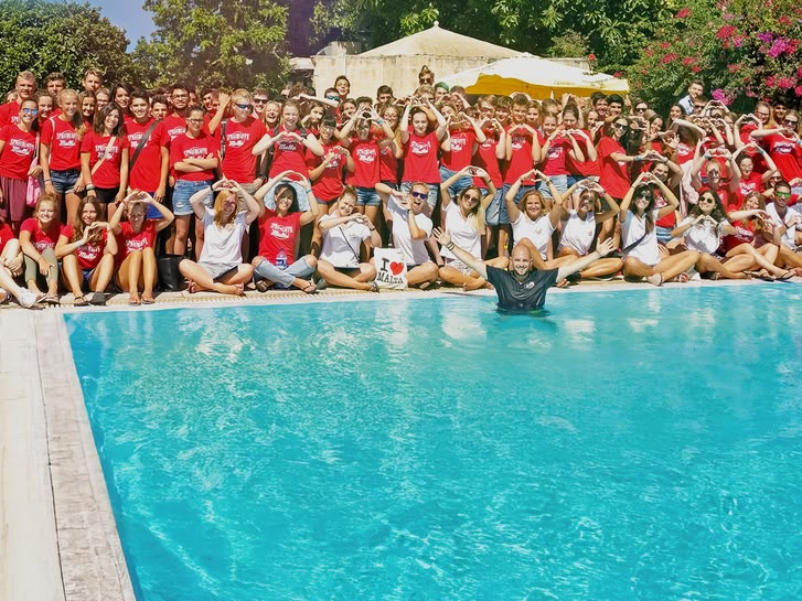 Large group of Sprachcaffe junior students in Malta posing by the poolside, many forming heart shapes with their hands.