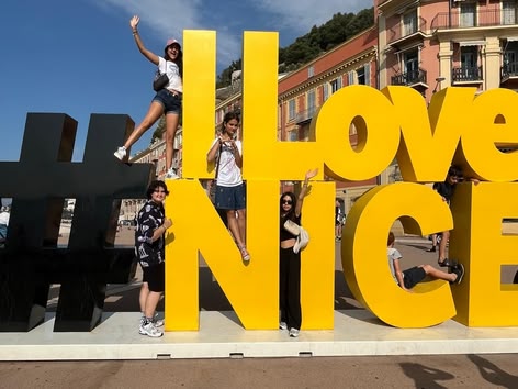 Eine Gruppe junger Menschen posiert an einem sonnigen Tag auf und um das große gelbe "#ILoveNICE"-Schild in Nizza, Frankreich.
