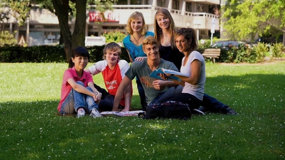 Eine Gruppe von Sprachcaffe-Juniorschülern sitzt auf der Wiese in Frankfurt, Deutschland, und genießt den sonnigen Tag.