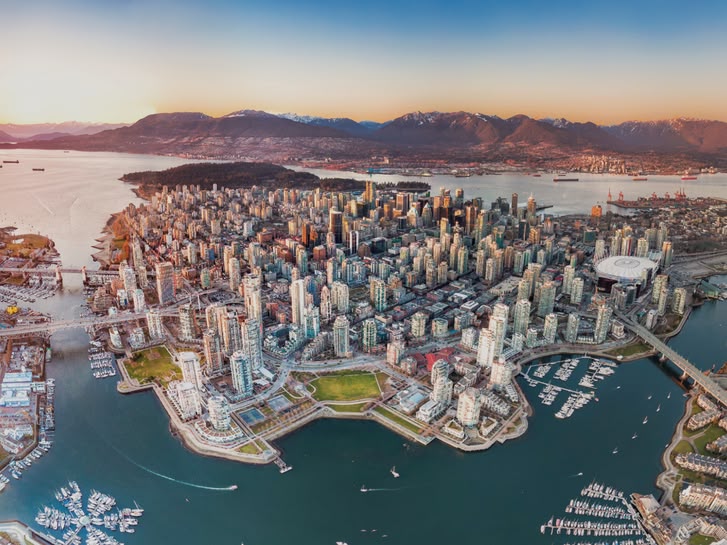 Aerial view of downtown Vancouver, Canada, with surrounding mountains, harbours, and bridges at sunset.