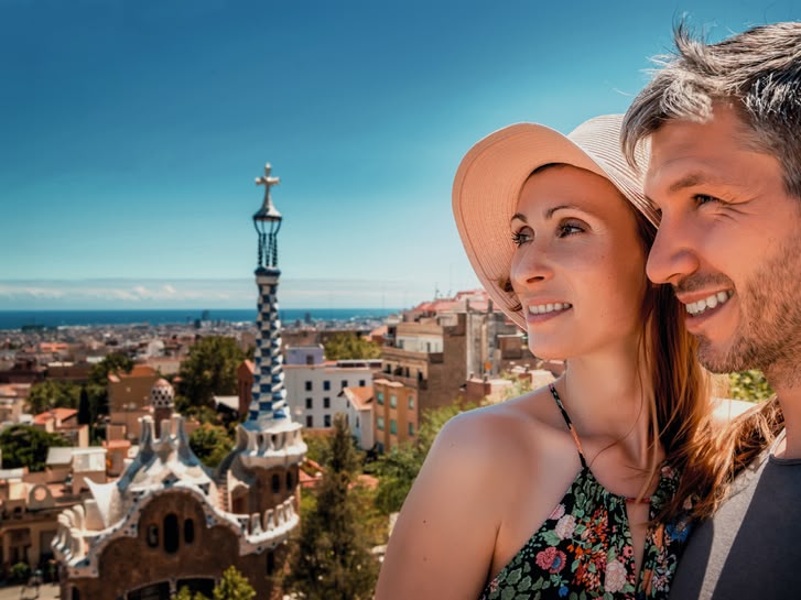 Ein lächelndes Paar genießt die Aussicht vom Park Güell in Barcelona, Spanien, mit der Stadt und dem Meer im Hintergrund.