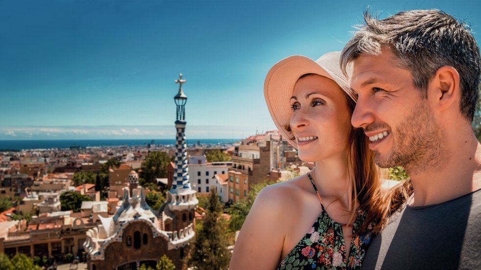 Ein lächelndes Paar genießt die Aussicht vom Park Güell in Barcelona, Spanien, mit der Stadt und dem Meer im Hintergrund.