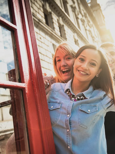Smiling girl posing by a red phone booth in London with Big Ben visible in the background.