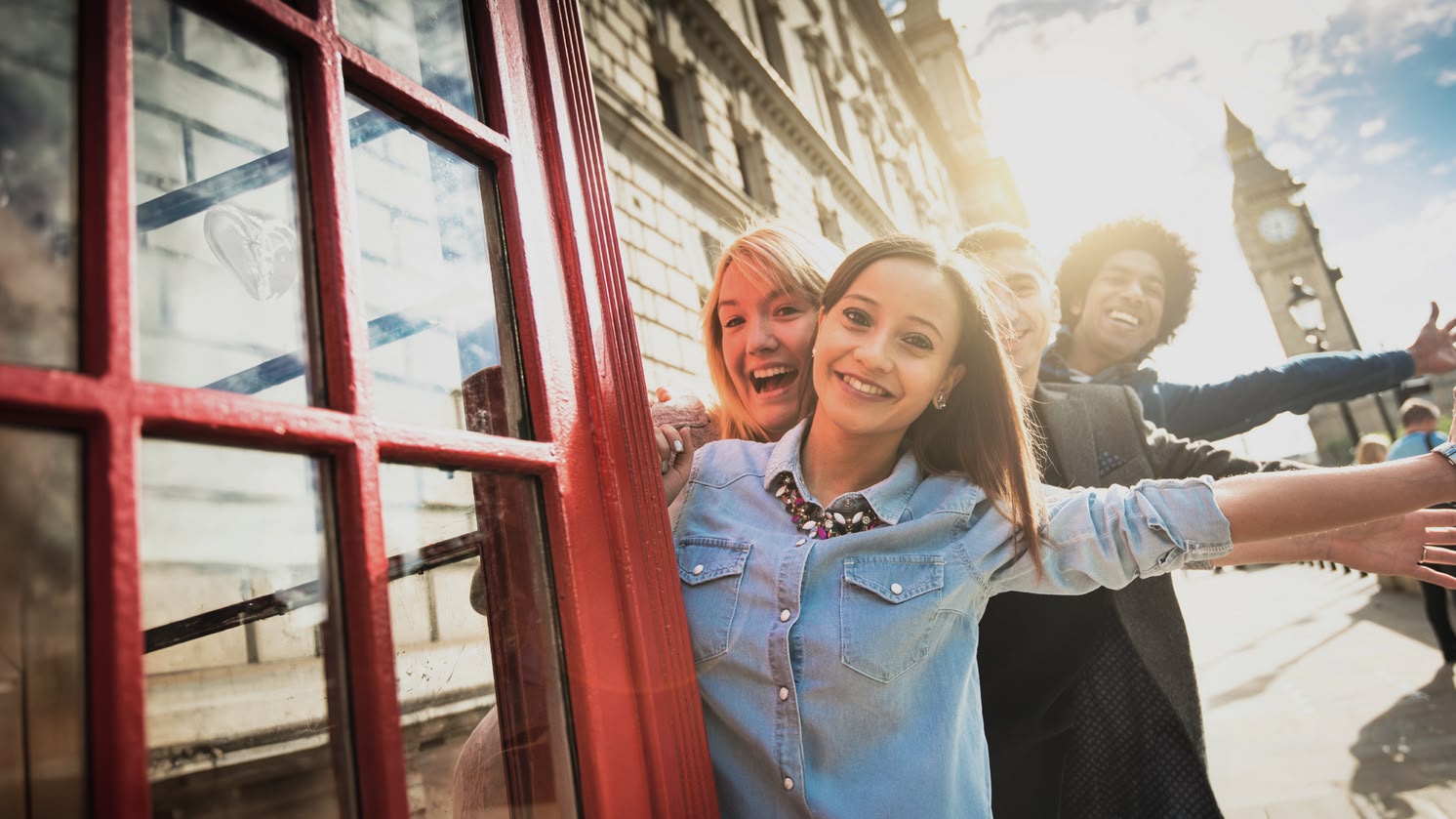Ein lächelndes Mädchen posiert vor einer roten Telefonzelle in London, mit dem Big Ben im Hintergrund.