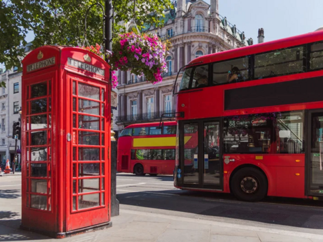 Klassische rote Londoner Telefonzelle und Doppeldeckerbusse auf einer Stadtstraße.