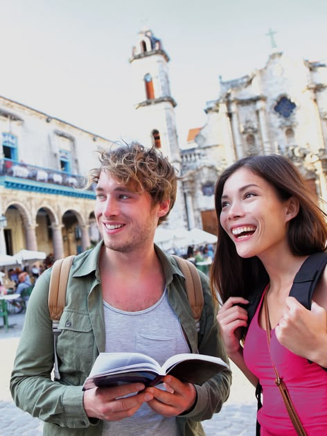 Two tourists exploring Old Havana, Cuba, holding a guidebook and smiling in a historic square with colonial architecture.