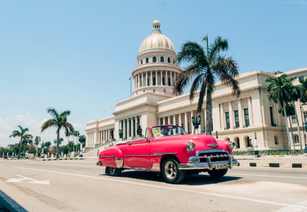 Klasyczny samochód przejeżdża przed budynkiem Kapitolu w Hawanie, Kuba, łącząc historyczny urok z tropikalnym klimatem miasta.