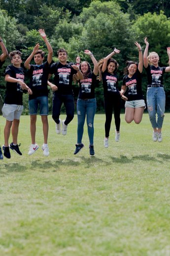 Sprachcaffe-Schülerinnen und -Schüler in England springen in der Luft auf einer grünen Wiese, tragen passende Shirts und genießen die freie Natur.