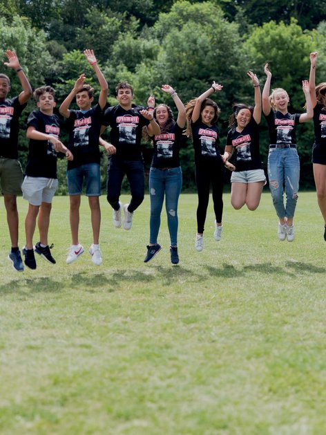 Sprachcaffe-Schülerinnen und -Schüler in England springen in der Luft auf einer grünen Wiese, tragen passende Shirts und genießen die freie Natur.