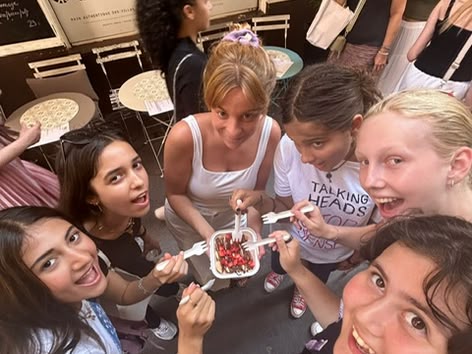 Eine Gruppe lächelnder Mädchen teilt sich ein Dessert auf einer Straße in Nizza, Frankreich, vor einem Café.