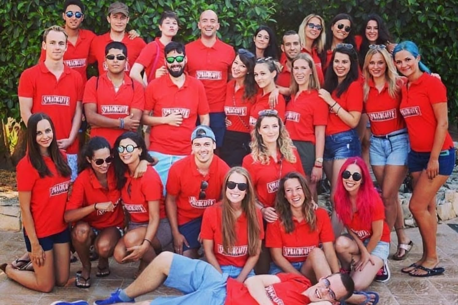 Eine Gruppe von Sprachcaffe-Mitarbeitern aus Malta posiert gemeinsam im Freien, alle tragen passende rote Sprachcaffe-Shirts.