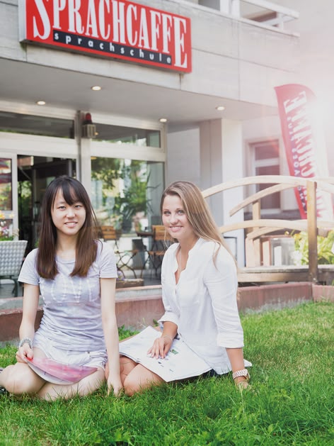 Two young women sitting on the grass in front of the Sprachcaffe language school in Frankfurt, Germany.