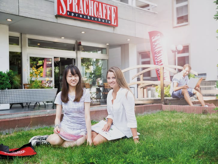 Two young women sitting on the grass in front of the Sprachcaffe language school in Frankfurt, Germany.