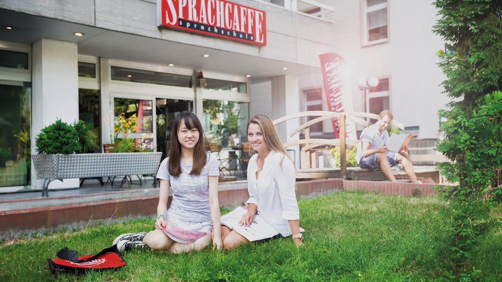 Zwei junge Frauen sitzen auf der Wiese vor der Sprachcaffe-Sprachschule in Frankfurt am Main.