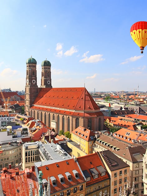 Aufdem Bild sind die Dächer von München zu sehen. Im Himmel befindet sich ein Heißluftballon.
