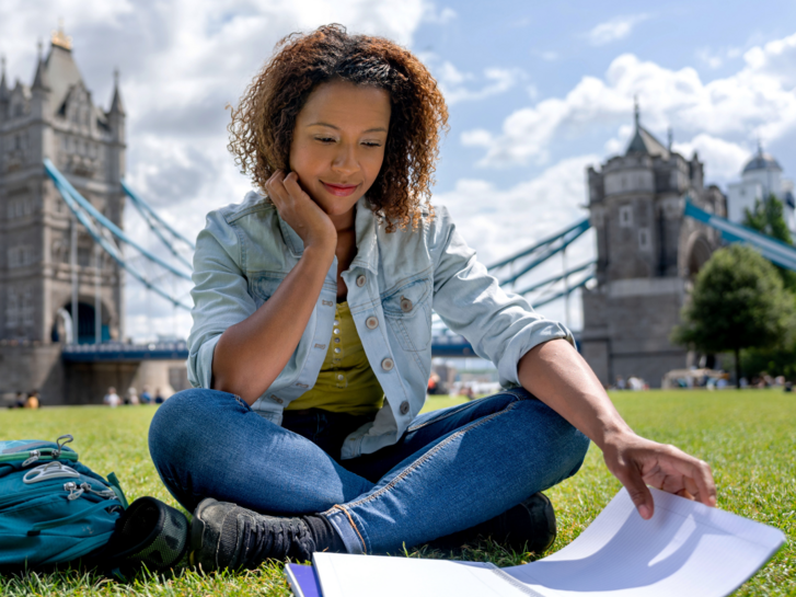 Englisch lernen macht Spaß, besonders in einem englischsprachigen Land. Hier lernt eine Frau auf der Wiese in London Englisch. Im Hintergrund ist die berühmte Tower Bridge.