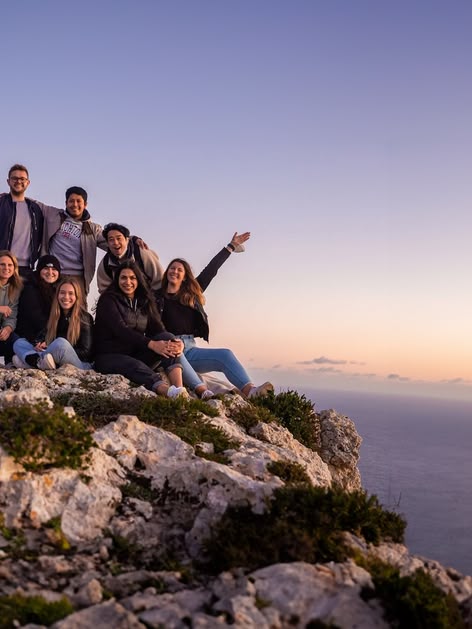 Group of young adults on a rocky cliff in Malta at sunset, overlooking the sea and enjoying the view.