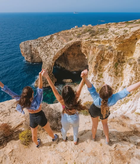 Drei Mädchen heben die Arme auf den Klippen mit Blick auf die Blaue Grotte.