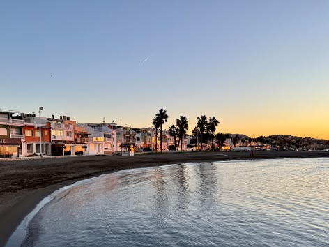 Blick auf den Sonnenuntergang am Strand von Pedregalejo in Málaga mit Palmen und Häusern am Meer.
